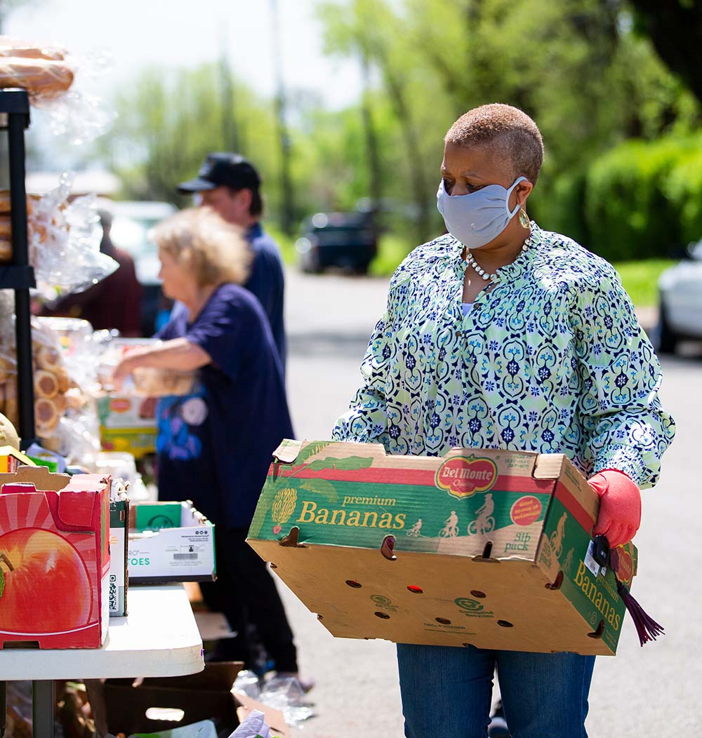 Woman carries food donation while wearing mask.
