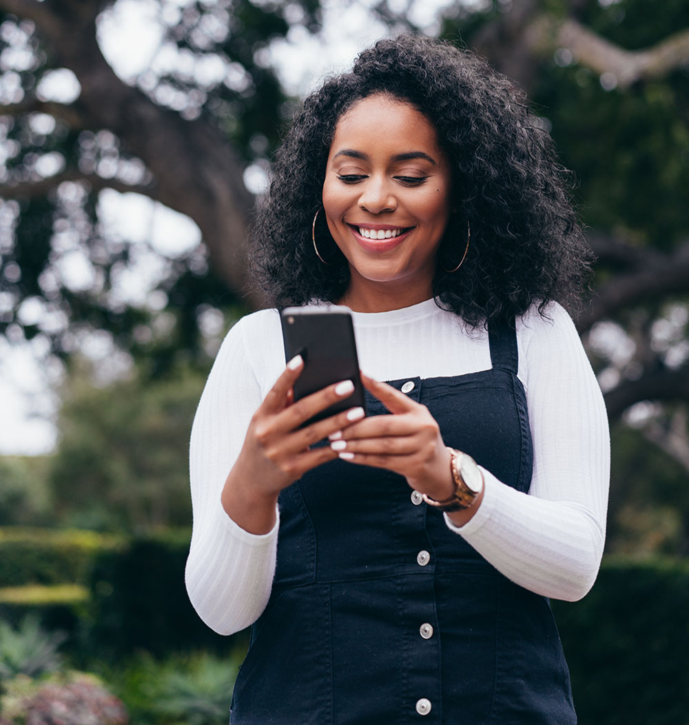 A woman smiling while using person to person pay on her phone.